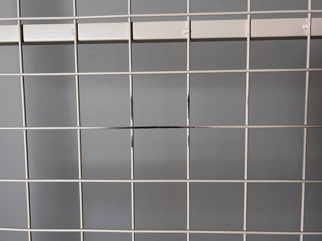 白い塗装のスチール網に付着した黒い塗料のような汚れ