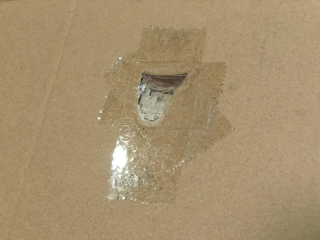 ぶつけてできた穴を透明テープで塞いだダンボール表面の写真