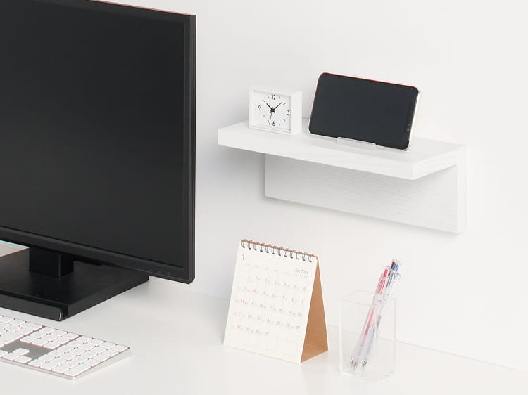 壁に付けられる家具棚にスマホと時計を置いてデスクで使う様子。