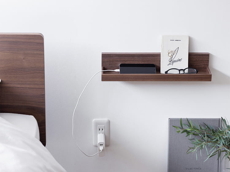 壁に付けられる家具トレーをベッドサイドに設置してスマホや眼鏡を置く様子。