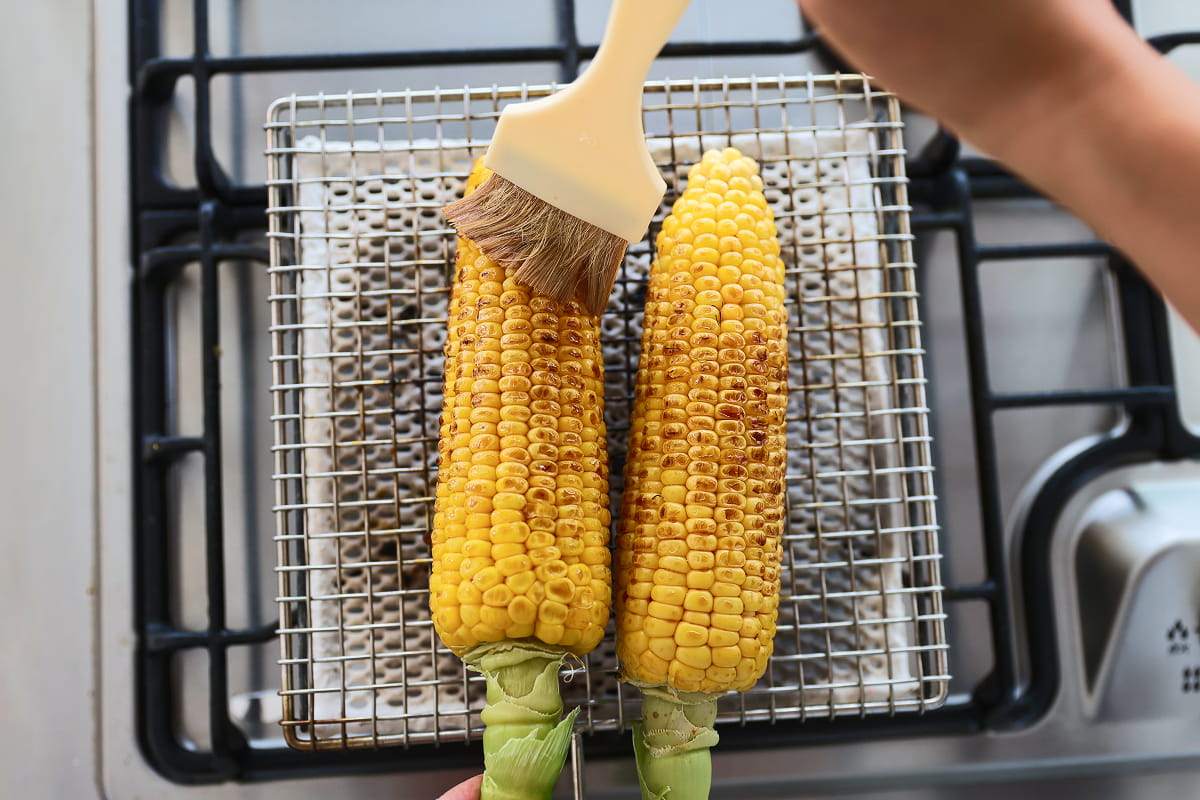 醤油を塗りながら焼かれているとうもろこしのイメージ画像