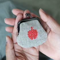 両手のひらにのせた生成地に赤いりんご刺繍のがま口