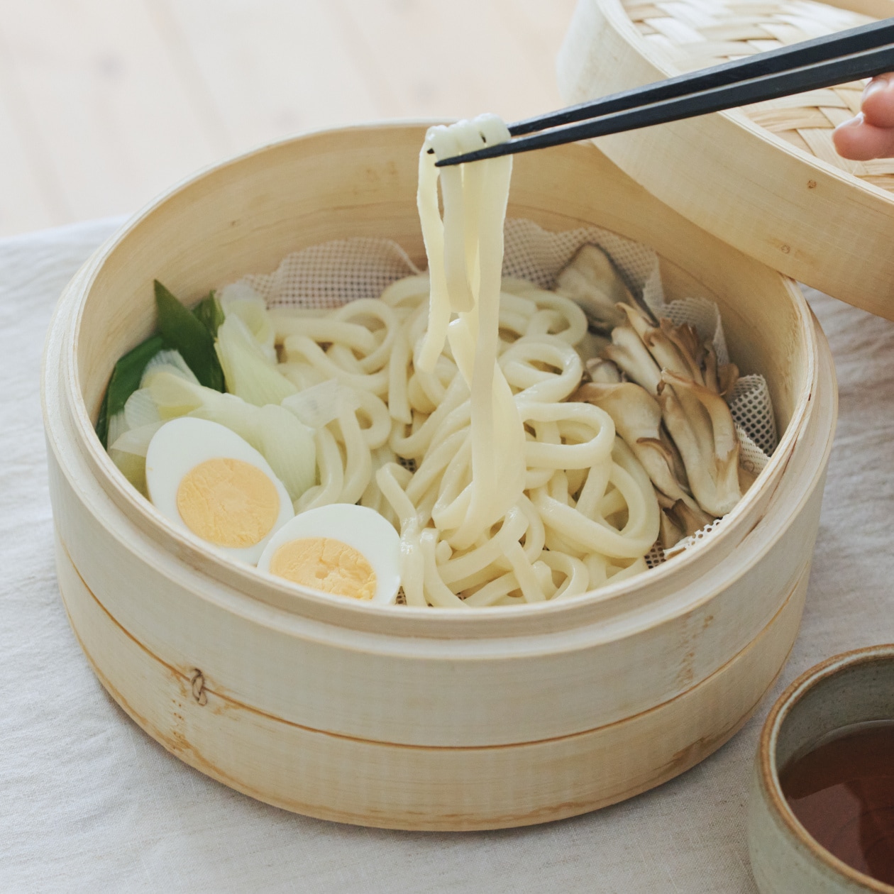 蒸篭で蒸しあげた冷凍うどんを箸でつまみ上げているところ