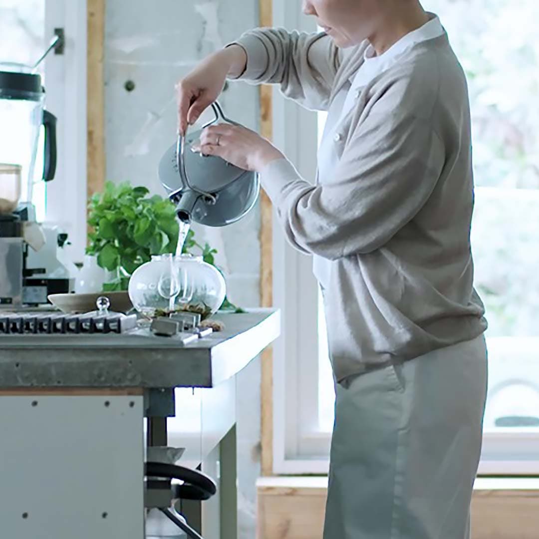 無印良品のカーディガンを羽織り、お茶を淹れる女性