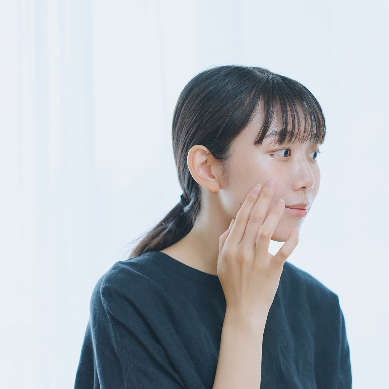 頬の質感を指で触れて確かめている女性