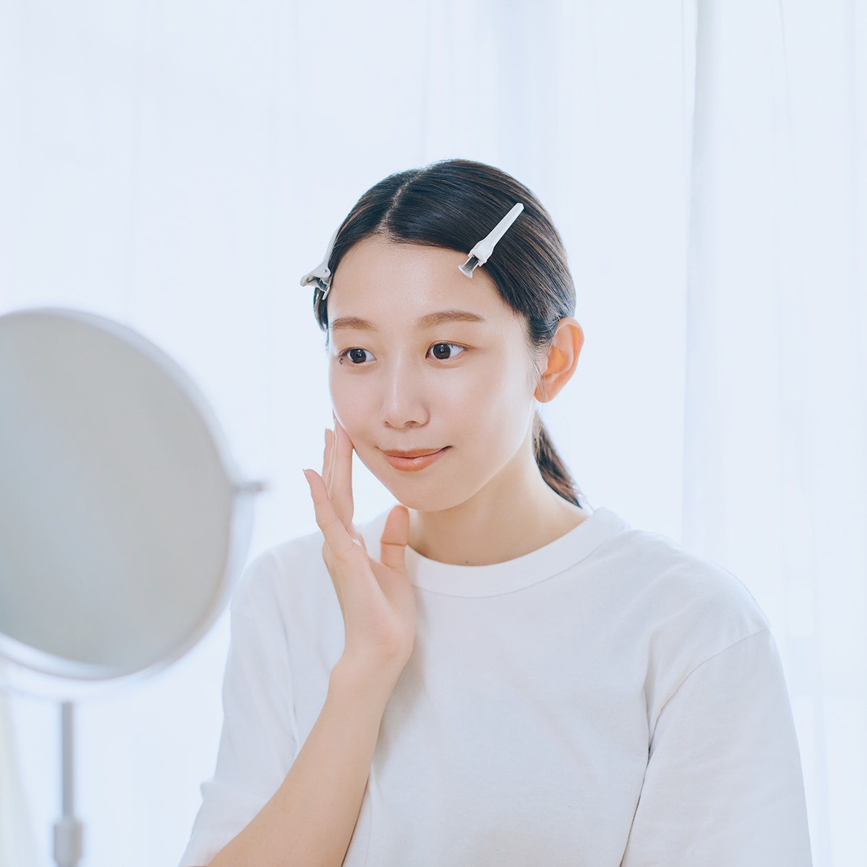 指で頬に触れ、鏡を見ている女性