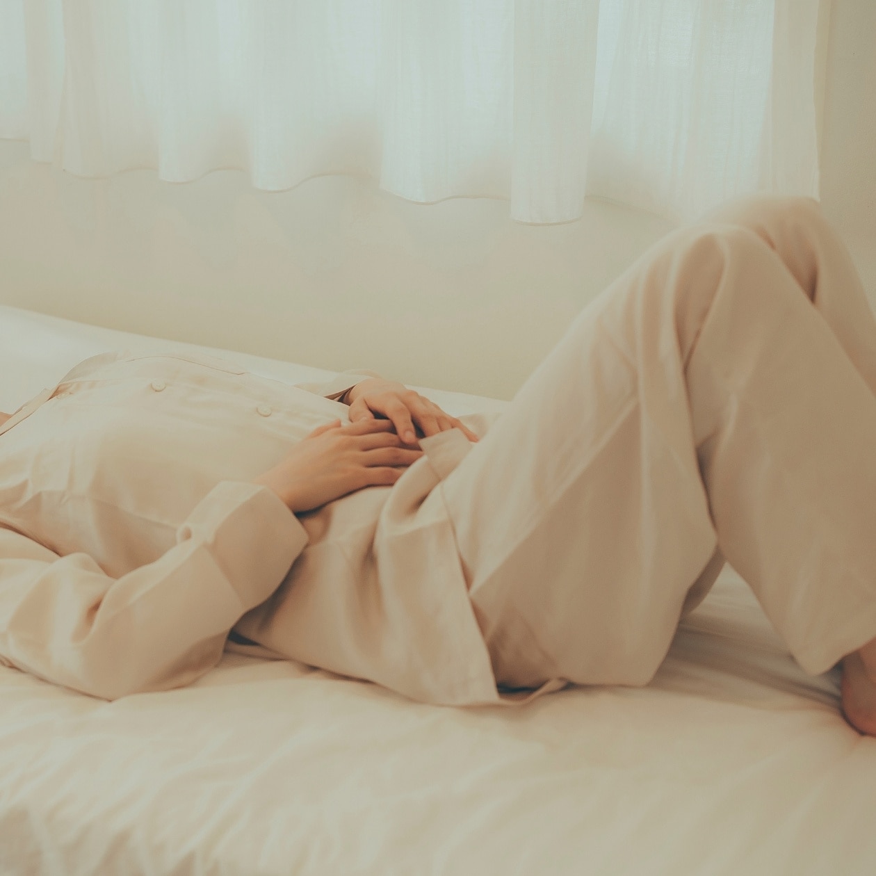 無印良品のパジャマをきて、ベッドで横になり腹式呼吸をする女性