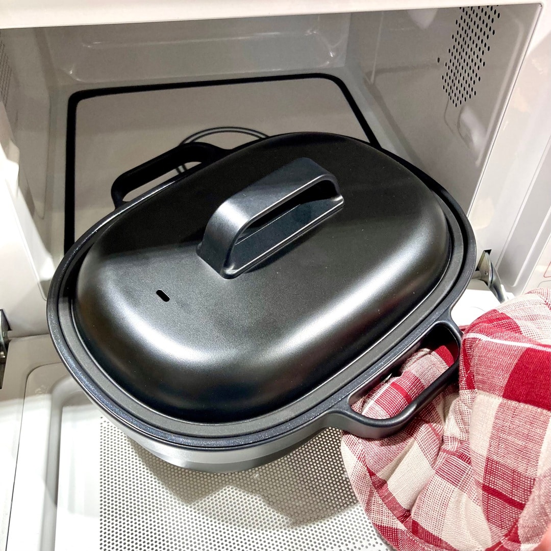 【テラスモール湘南】本記事で紹介する新商品「レンジで焼き料理　グリルプレート」の黒色版を、同じく商品の鍋つかみにもなる鍋敷き（赤チェック）を嵌めた手で持ち手をつかんで、電子レンジから取り出す写真