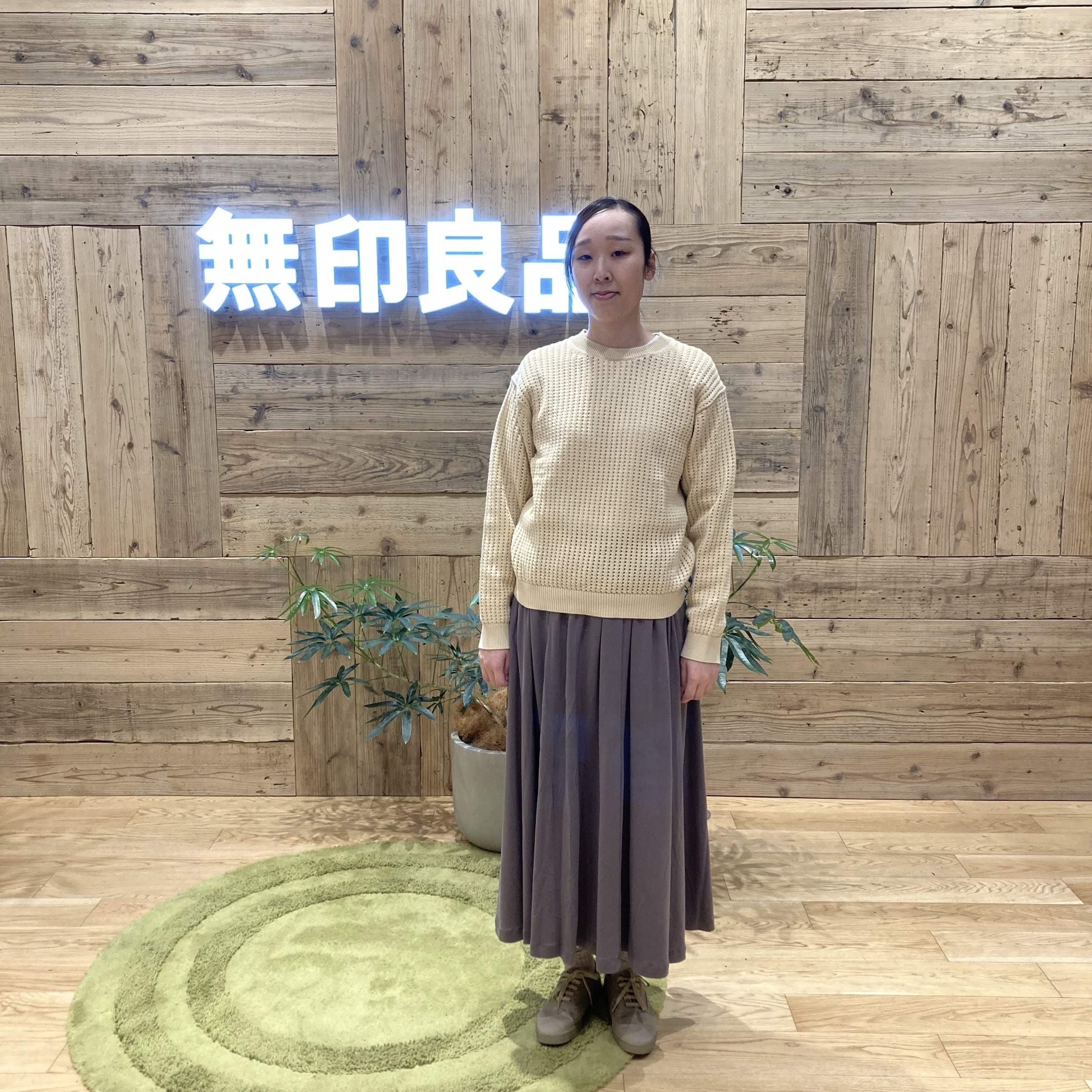 チャコールグレーのスカートと黄色のニットを着て立つ女性