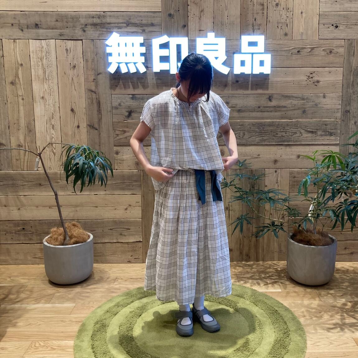 チェックのセットアップを着てうつむいて立つ女性