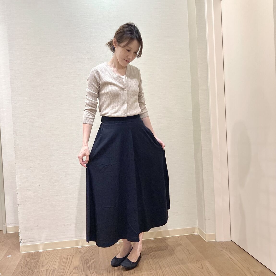 黒のフレアスカートとベージュのカーディガンを着用した女性