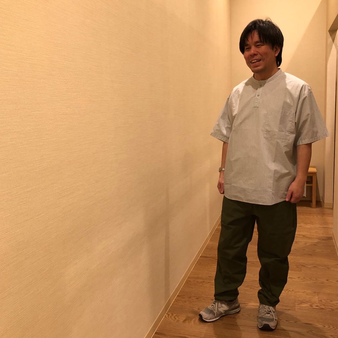 ヘンリーネックのシャツとカーキー色のパンツを着用した男性