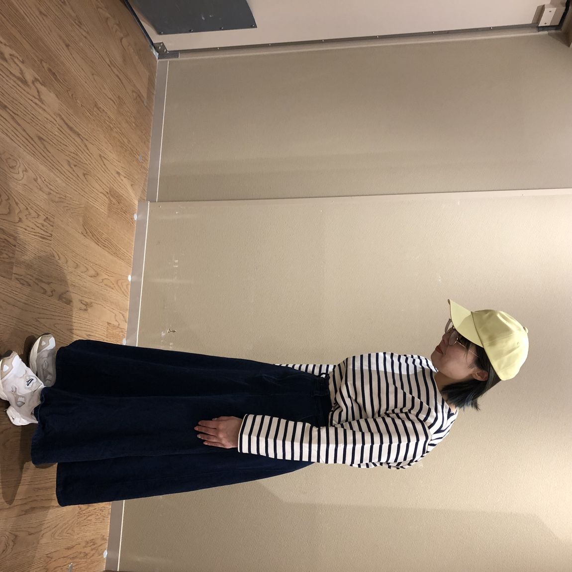 ボーダーのトップスとカポックデニムスカートを着用し、黄色いキャップをかぶっている女性の写真