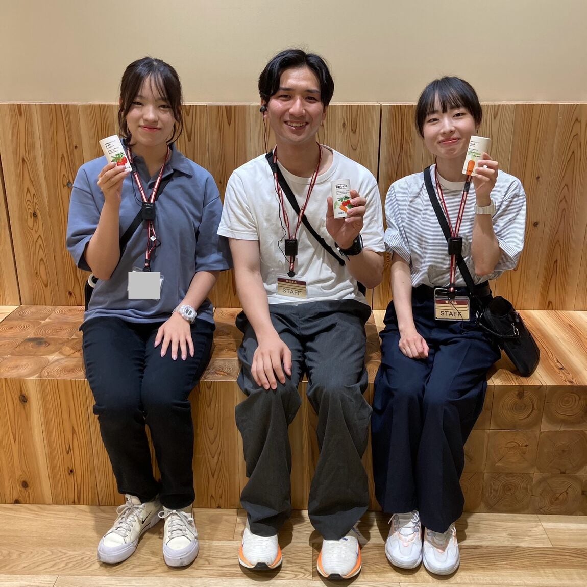 「国産野菜１００％ジュース」を持って微笑む3人のスタッフの画像