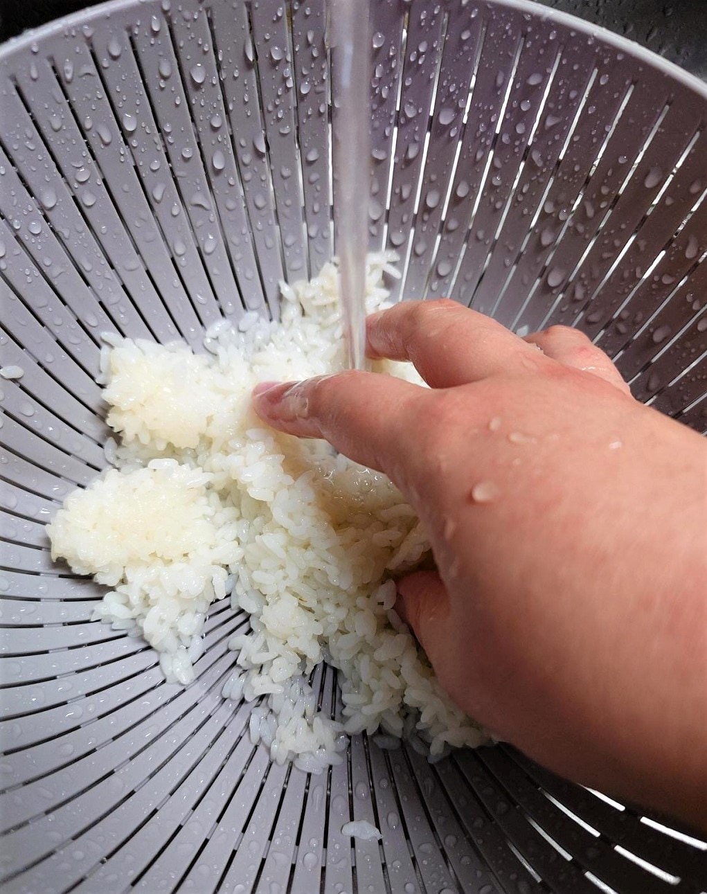 【テラスモール湘南】ざるに入れたあたたかいご飯を流水にさらし手で混ぜる写真