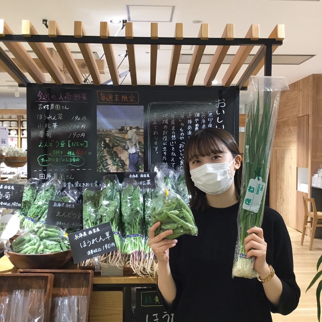 野菜売場でえんどう豆と青ネギを持ったスタッフの写真