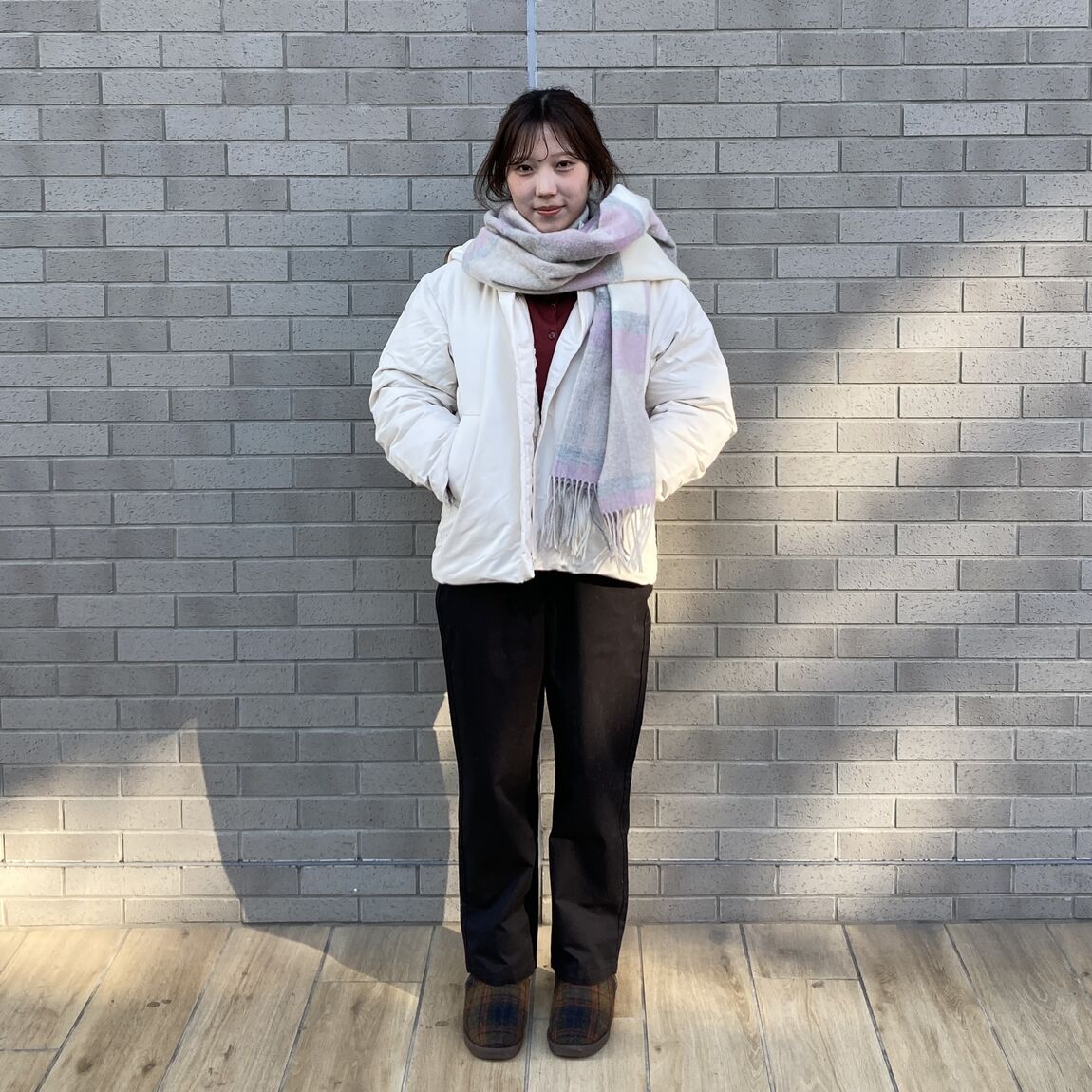 白いジャケット、ピンクとグレーのマフラー、赤いセーター、黒いパンツの女性