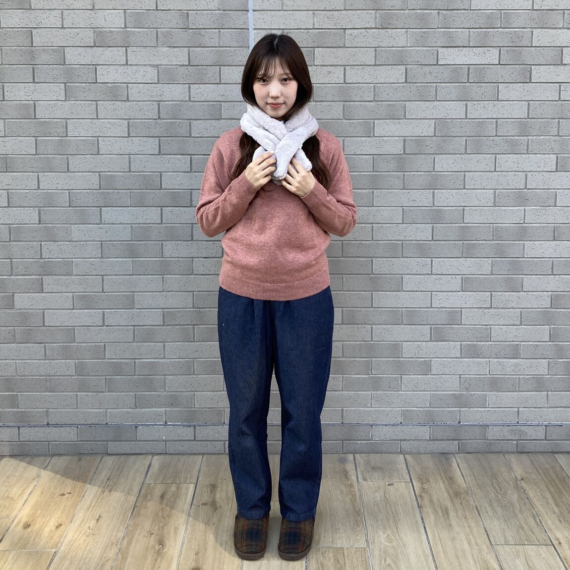 ピンクのセーター、白いボアマフラー、デニムパンツの女性