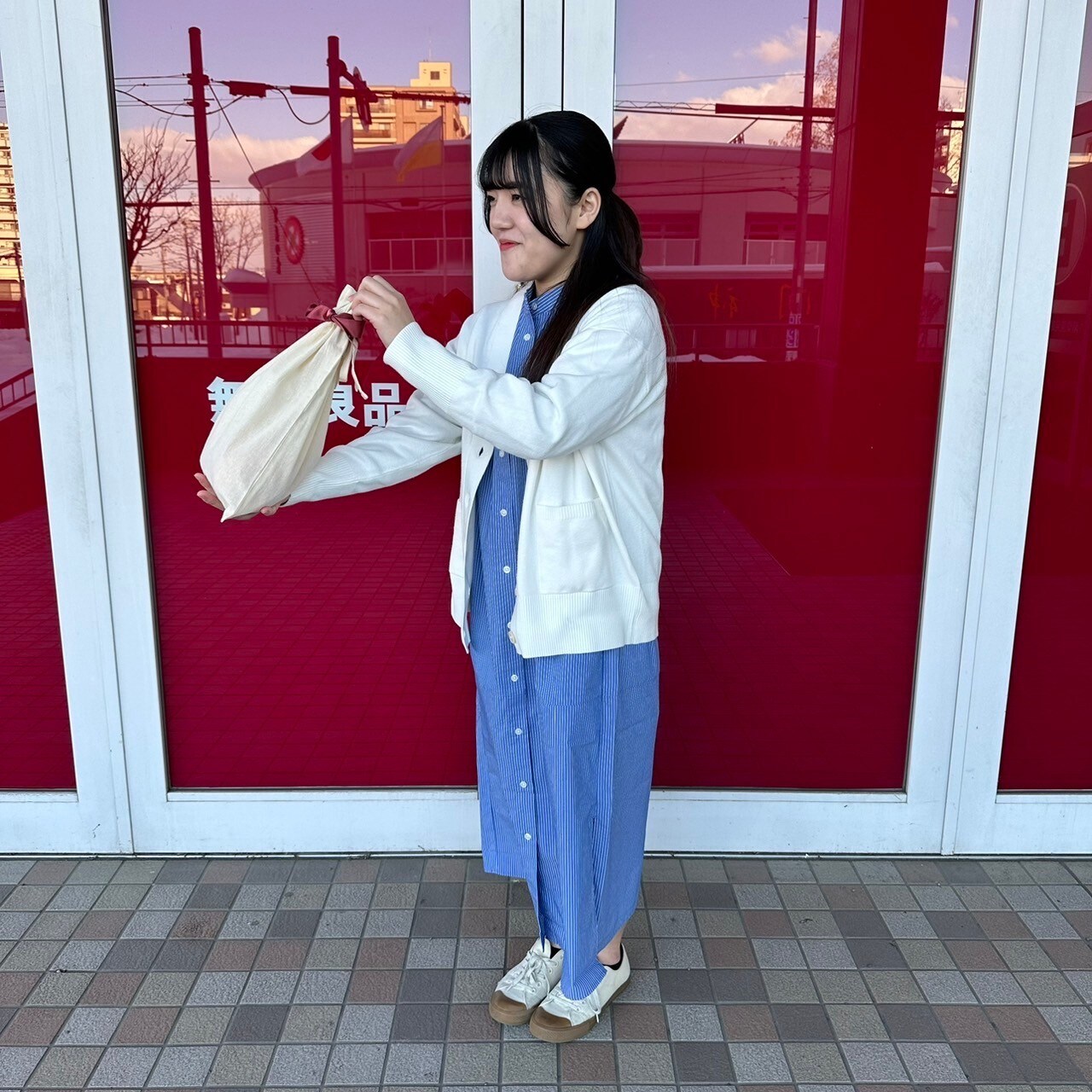 ギフト袋を差し出すスタンドカラーワンピースを着た女性スタッフ