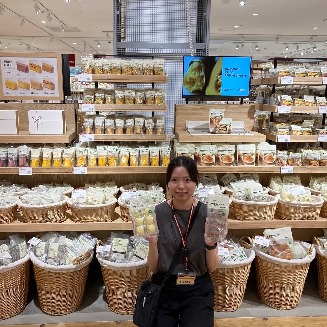 お菓子売り場の前で、お菓子を持って微笑むスタッフの写真