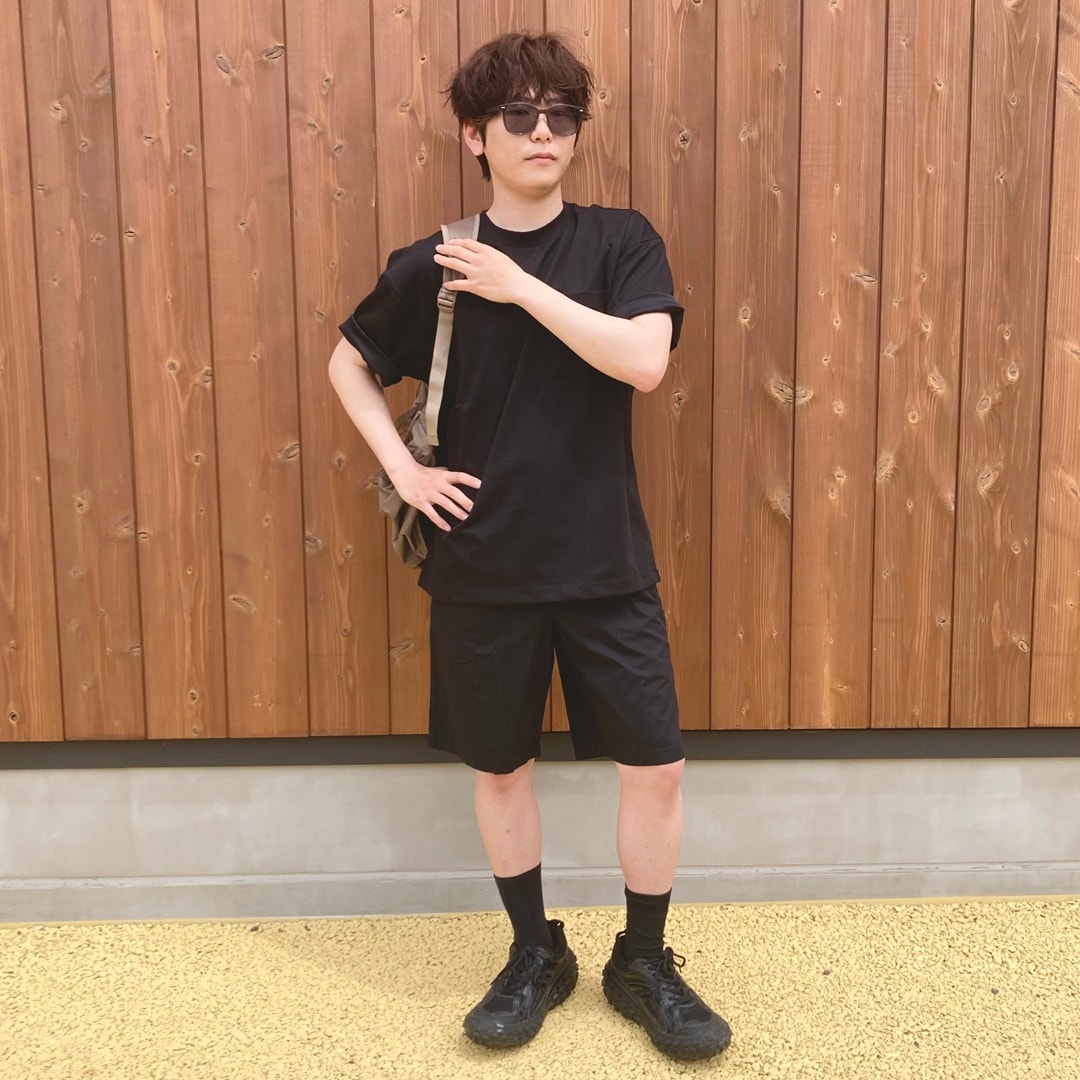 黒の半袖Tシャツとショートパンツを着用し、リュックを肩にかけているスタッフ。