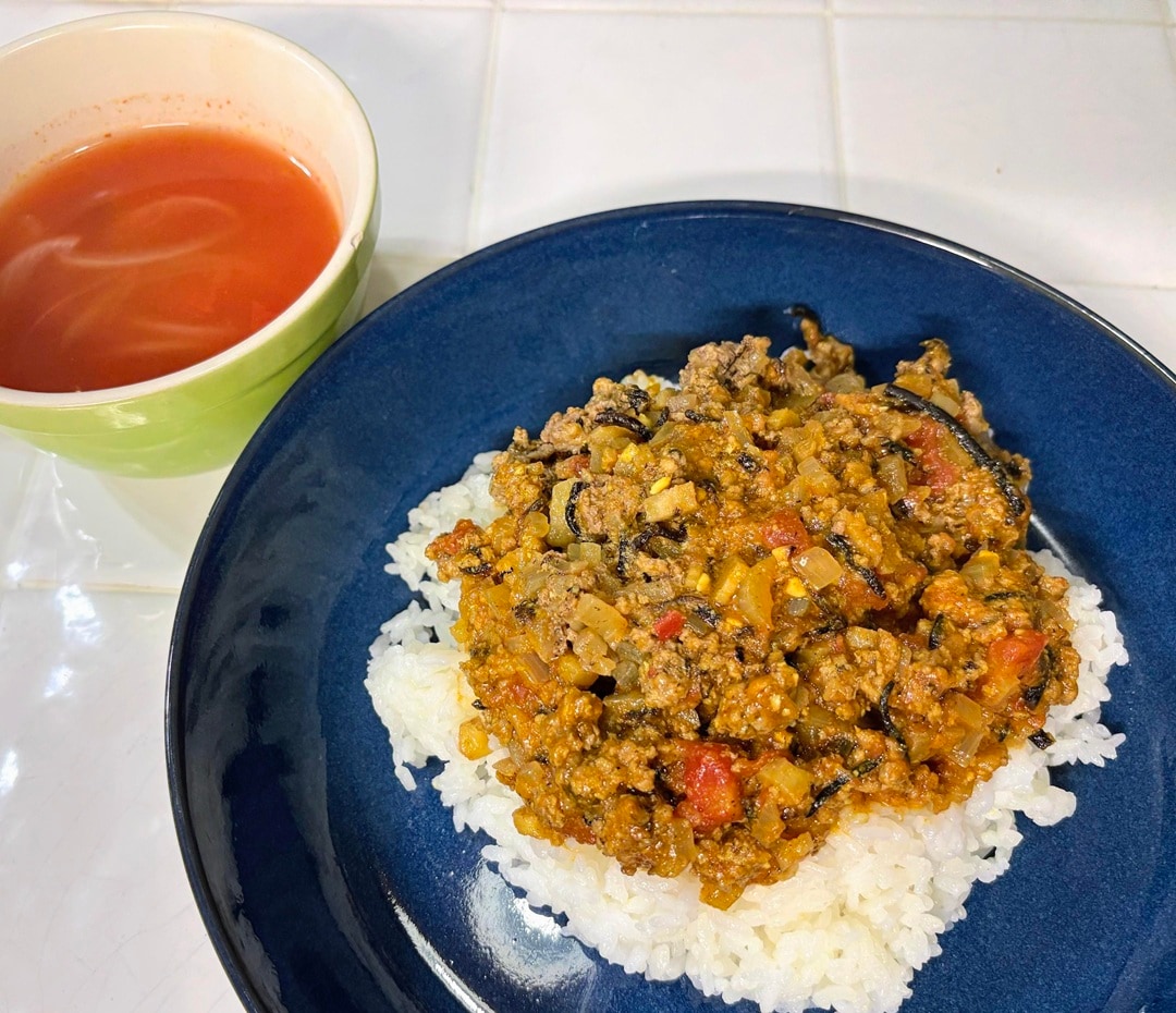 【テラスモール湘南】グリルプレートで作ったキーマカレールーをごはんと合わせて盛り付けた紺色のお皿と、トマトスープが入った黄緑色のマグが並んだ食卓の写真