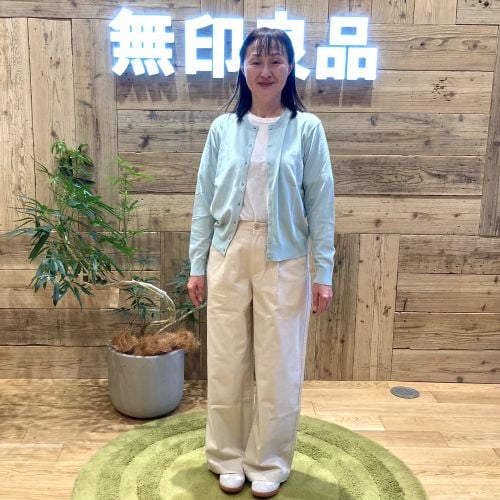 ライトブルーのカーディガンに白のパンツをはいて立つ女性