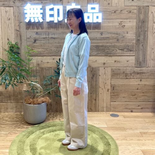 ライトブルーのカーディガンに白のパンツをはいて斜めを向いて立つ女性