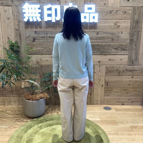ライトブルーのカーディガンに白のパンツをはいて後ろ向きに立つ女性
