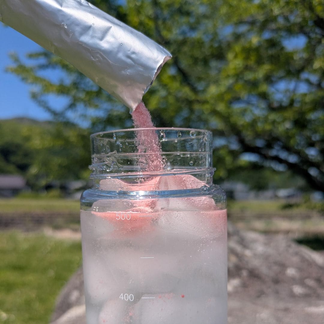 ピンク色をした粉末を水の入ったボトルに入れている写真
