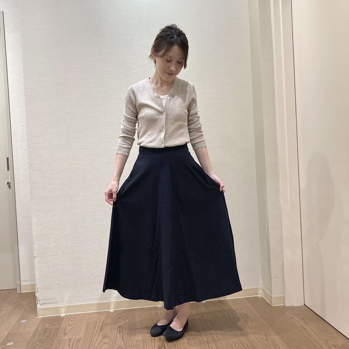 黒のフレアスカートとベージュのカーディガンを着用した女性