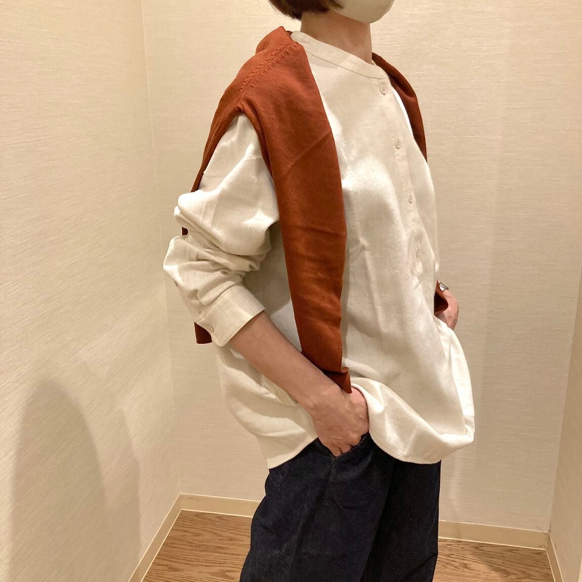 アイボリーのスタンダードシャツにブラウンのカーディガンを肩にかけた女性