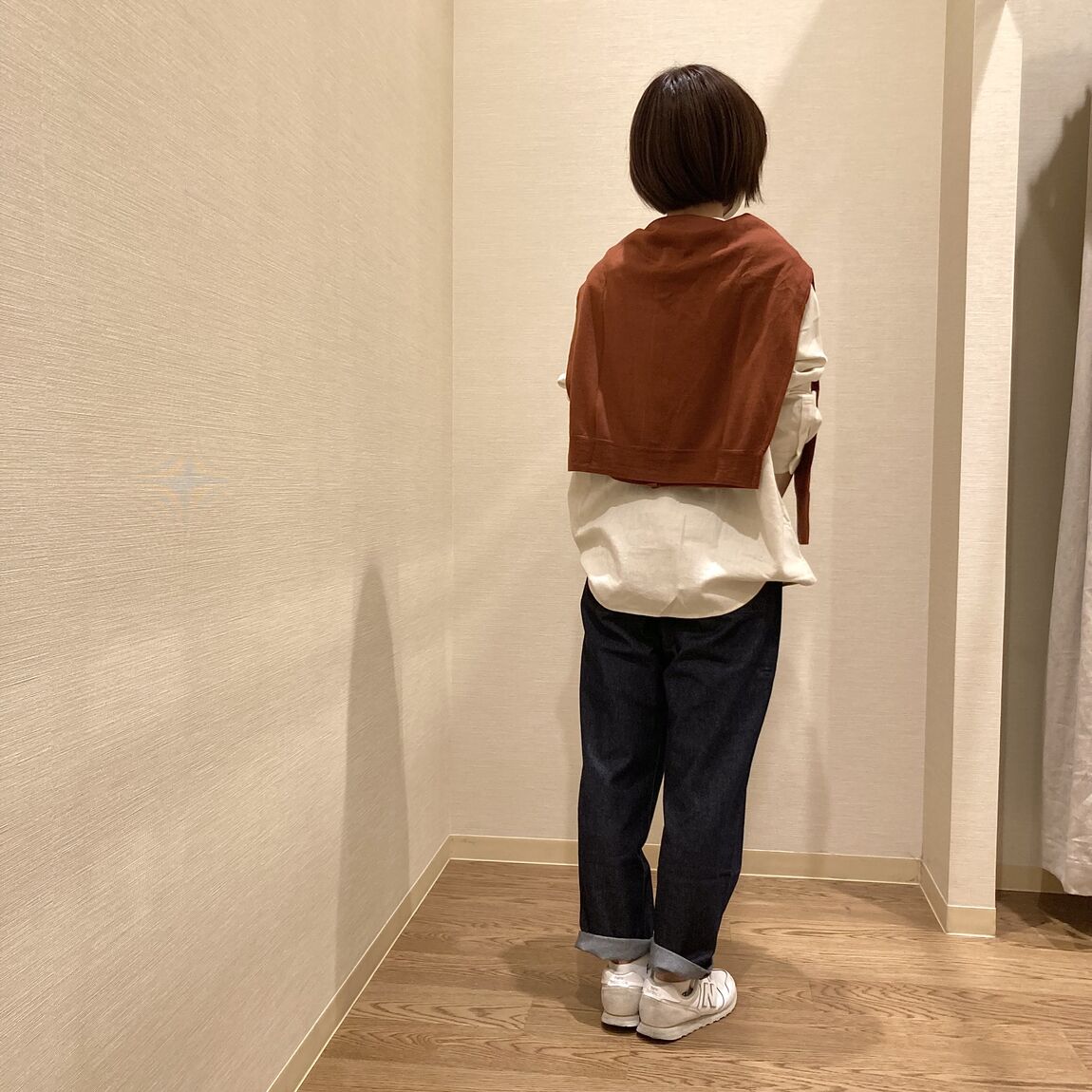 アイボリーのスタンダードシャツにブラウンのカーディガンを肩にかけた女性