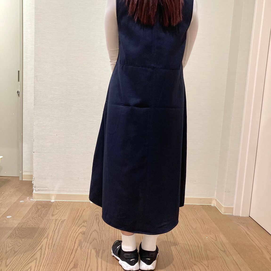 ネイビーのワンピースにピンクのセーターを肩がけした着用した女性