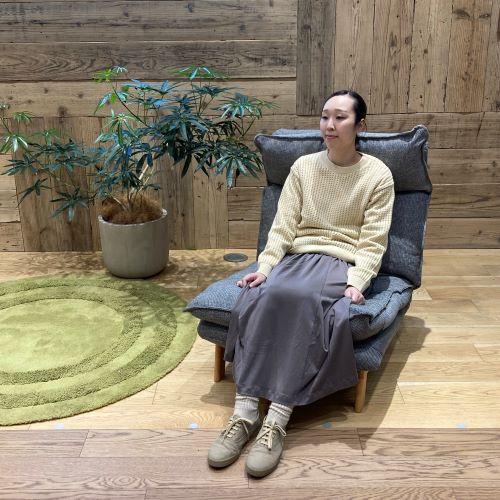 チャコールグレーのスカートと黄色のニットを着て椅子に座る女性