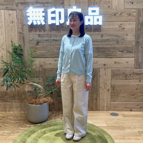 ライトブルーのカーディガンに白のパンツをはいて立つ女性