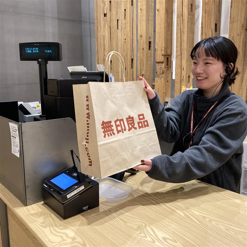 女性が無印良品の紙袋を持ち、お客様へ渡している画像
