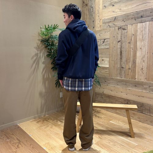 ネイビーのトレーナーにブラウンのパンツをはいて後ろ向きに立つ男性