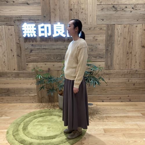 チャコールグレーのスカートと黄色のニットを着て横を向いて立つ女性